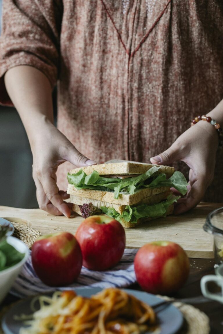 Crop anonymous female in casual dress standing near dinging table and touching tasty healthy sandwich in kitchen