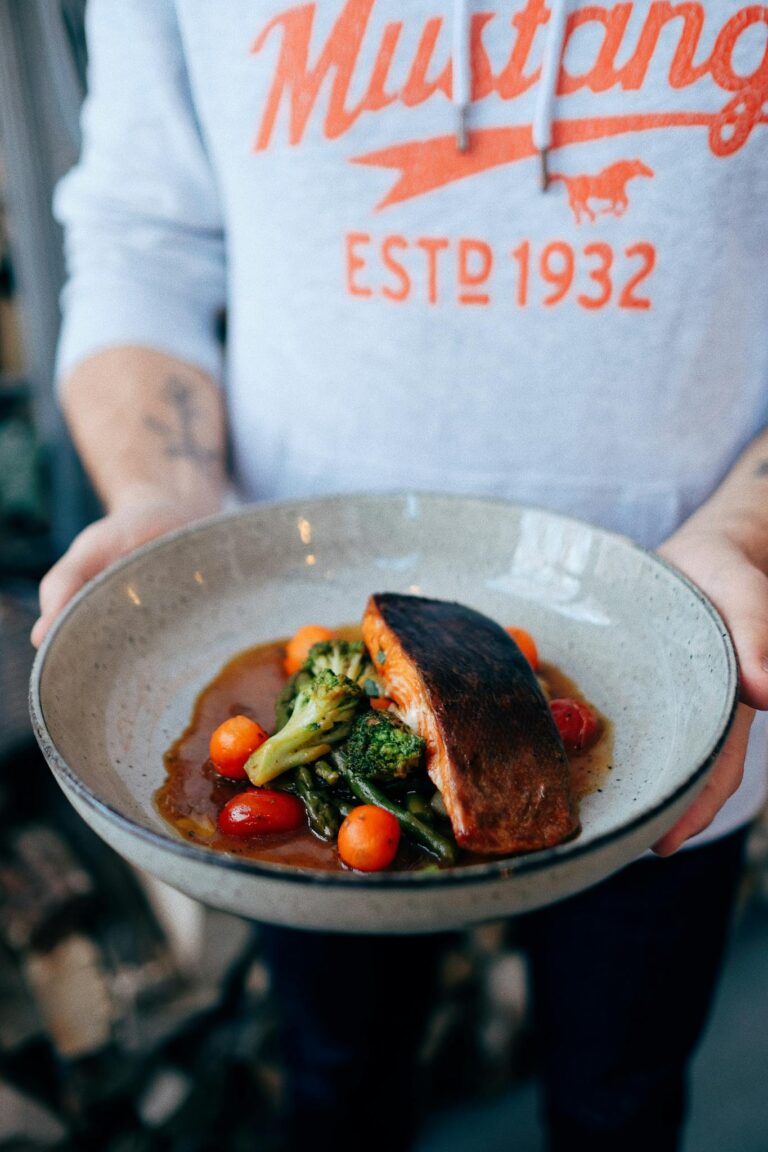 Crop anonymous young man in casual clothes holding plate with delicious teriyaki salmon with broccoli and cherry tomatoes